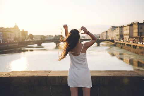 Italy, Florence, back view of woman wearing white summer dress standing on a bridge at sunset stock photo