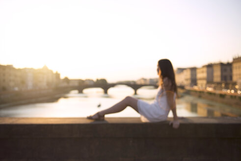 Italien, Florenz, Frau im weißen Sommerkleid auf einer Brücke bei Sonnenuntergang sitzend - GEMF000329