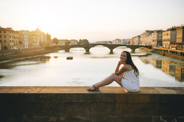 Italien, Florenz, glückliche Frau sitzt auf einer Brücke bei Sonnenuntergang - GEMF000332