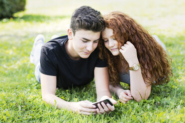 Teenager-Paar liegt auf einer Wiese und schaut auf sein Smartphone - GDF000855