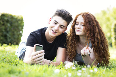Teenager-Paar liegt auf einer Wiese und schaut auf sein Smartphone - GDF000856