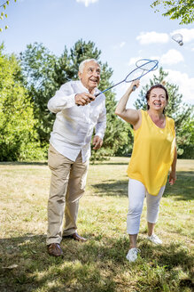 Glückliches älteres Paar auf einer Wiese beim Badminton spielen - RKNF000192