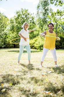 Fröhliche reife Frauen beim Üben mit Hula-Hoop-Reifen auf einer Wiese - RKNF000193