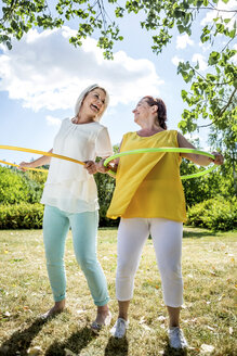 Glückliche reife Frauen mit Hula-Hoop-Reifen auf einer Wiese - RKNF000194