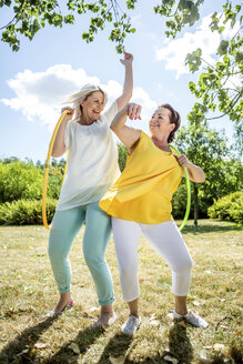 Glückliche reife Frauen mit Hula-Hoop-Reifen auf einer Wiese - RKNF000195