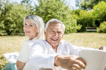 Smiling elderly couple on meadow reading books - RKNF000199