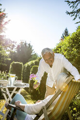 Ein älterer Mann schenkt einer Frau im Garten eine Blume - RKNF000230