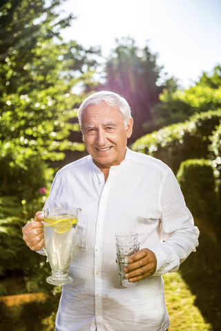 Lächelnder älterer Mann hält Karaffe mit Wasser im Garten, lizenzfreies Stockfoto