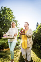 Two happy mature women carrying apples and tray in garden - RKNF000252