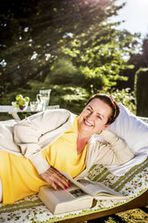 Lächelnde reife Frau beim Lesen eines Buches in der Gartenlounge - RKNF000255