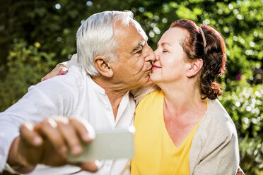 Elderly couple kissing and taking selfie outdoors - RKNF000267