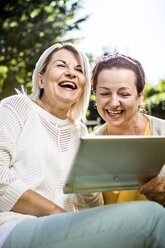 Glückliche reife Frauen im Garten mit digitalem Tablet - RKNF000272