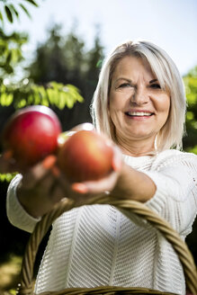 Smiling mature woman holding apples outdoors - RKNF000282