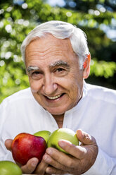 Lächelnder älterer Mann hält Äpfel im Freien - RKNF000287