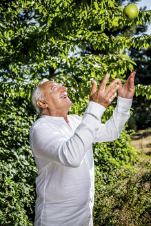 Lächelnder älterer Mann, der einen Apfel in den Garten wirft - RKNF000288