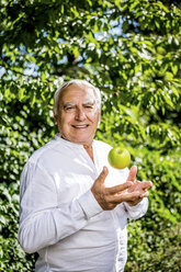 Lächelnder älterer Mann mit Apfel im Garten - RKNF000289