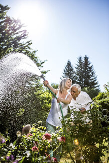 Lächelnde reife Frau gießt Blumen im Garten mit Mann küsst ihre Schulter - RKNF000293
