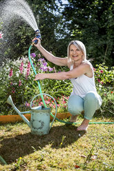 Smiling mature woman watering flowers in garden - RKNF000296