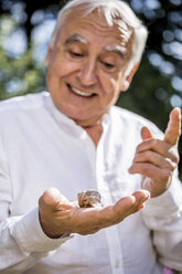 Smiling senior man with snail in his hand - RKNF000302