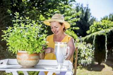 Lächelnde reife Frau, die sich um eine Topfpflanze im Garten kümmert - RKNF000309