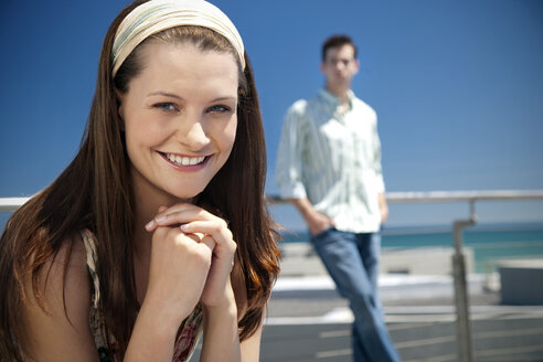 Porträt einer lächelnden jungen Frau mit einem Mann im Hintergrund - TOYF001331