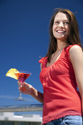 Lächelnde junge Frau im Sonnenschein mit Getränk in der Hand - TOYF001384