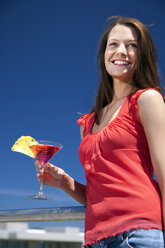 Smiling young woman in sunshine holding drink - TOYF001384