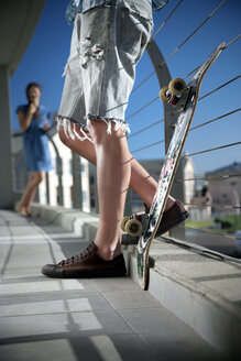 Junger Mann mit Skateboard auf Balkon und Frau im Hintergrund - TOYF001355