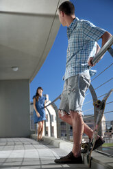 Junger Mann mit Skateboard auf Balkon mit Blick auf Frau - TOYF001356