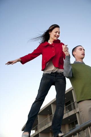 Young man supporting girlfriend balancing on railing stock photo