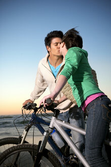 Junges Paar küsst sich auf Fahrrädern an der Küste - TOYF001396