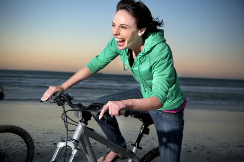 Unbekümmerte junge Frau auf Mountainbike am Strand - TOYF001397