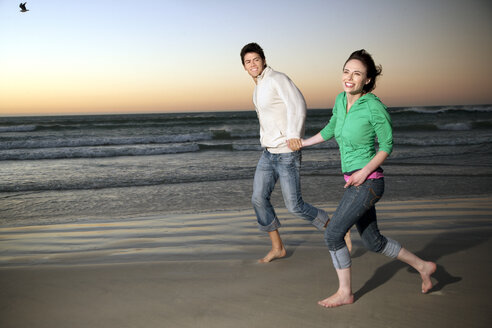 Junges Paar läuft Hand in Hand am Strand in der Abenddämmerung - TOYF001370