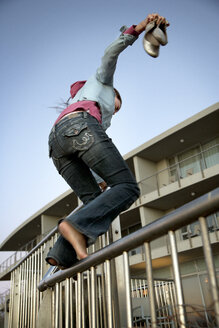 Junge Frau balanciert mit nackten Füßen auf einem Geländer - TOYF001372
