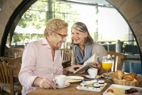 Lächelndes älteres Ehepaar liest ein Buch und frühstückt in einem Café, lizenzfreies Stockfoto