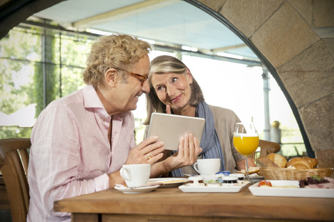 Lächelndes älteres Paar mit digitalem Tablet beim Frühstück in einem Café, lizenzfreies Stockfoto