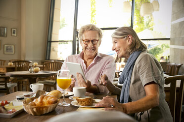 Smiling senior couple with digital tablet having breakfast in a cafe - TOYF001267