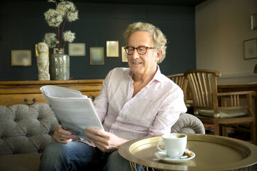 Smiling senior man in lounge room reading magazine - TOYF001275