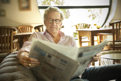 Smiling senior man in lounge room reading newspaper stock photo