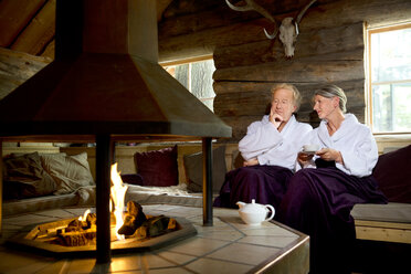Senior couple wearing bathrobes sitting at the fireplace - TOYF001287