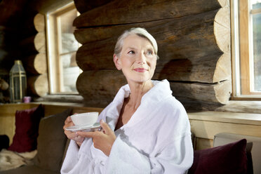 Lächelnde ältere Frau im Bademantel trinkt Tee - TOYF001294