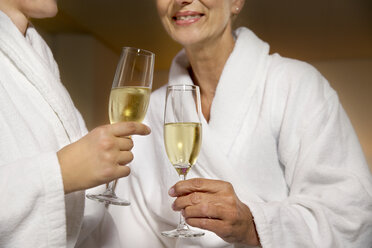Two women in bathrobes clinking champagne glasses - TOYF001320