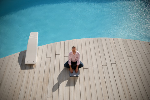 Spanien, Mallorca, Mann sitzt vor einem Pool und benutzt einen Laptop, lizenzfreies Stockfoto