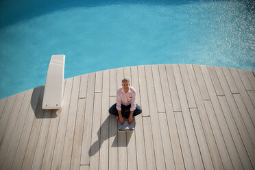 Spain, Mallorca, man sitting in front of a pool using laptop - TOYF001170