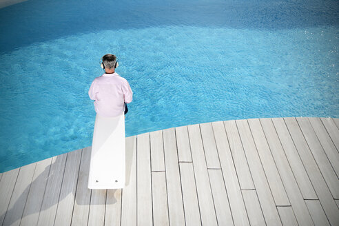 Spanien, Mallorca, Rückenansicht eines Mannes, der auf dem Sprungbrett eines Pools sitzt und mit Kopfhörern Musik hört - TOYF001175
