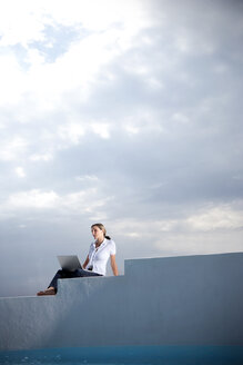 Spain, Mallorca, woman with laptop sitting on stairs besides in front of clouded sky - TOYF001181