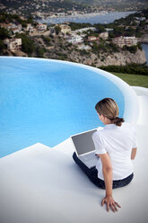 Spanien, Mallorca, Frau mit Laptop sitzt auf einer Treppe neben einem Schwimmbad - TOYF001183