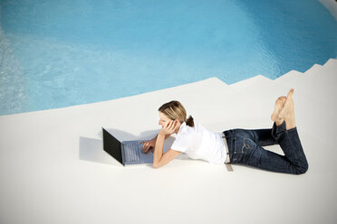 Spanien, Mallorca, Frau liegt neben einem Schwimmbad und schaut auf einen Laptop - TOYF001185