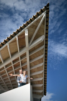 Glückliches Paar steht auf der Terrasse eines Hauses und genießt die Aussicht - TOYF001189