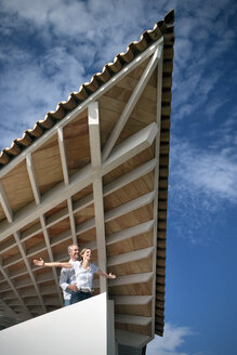 Happy couple standing on terrace of a house enjoying view - TOYF001189